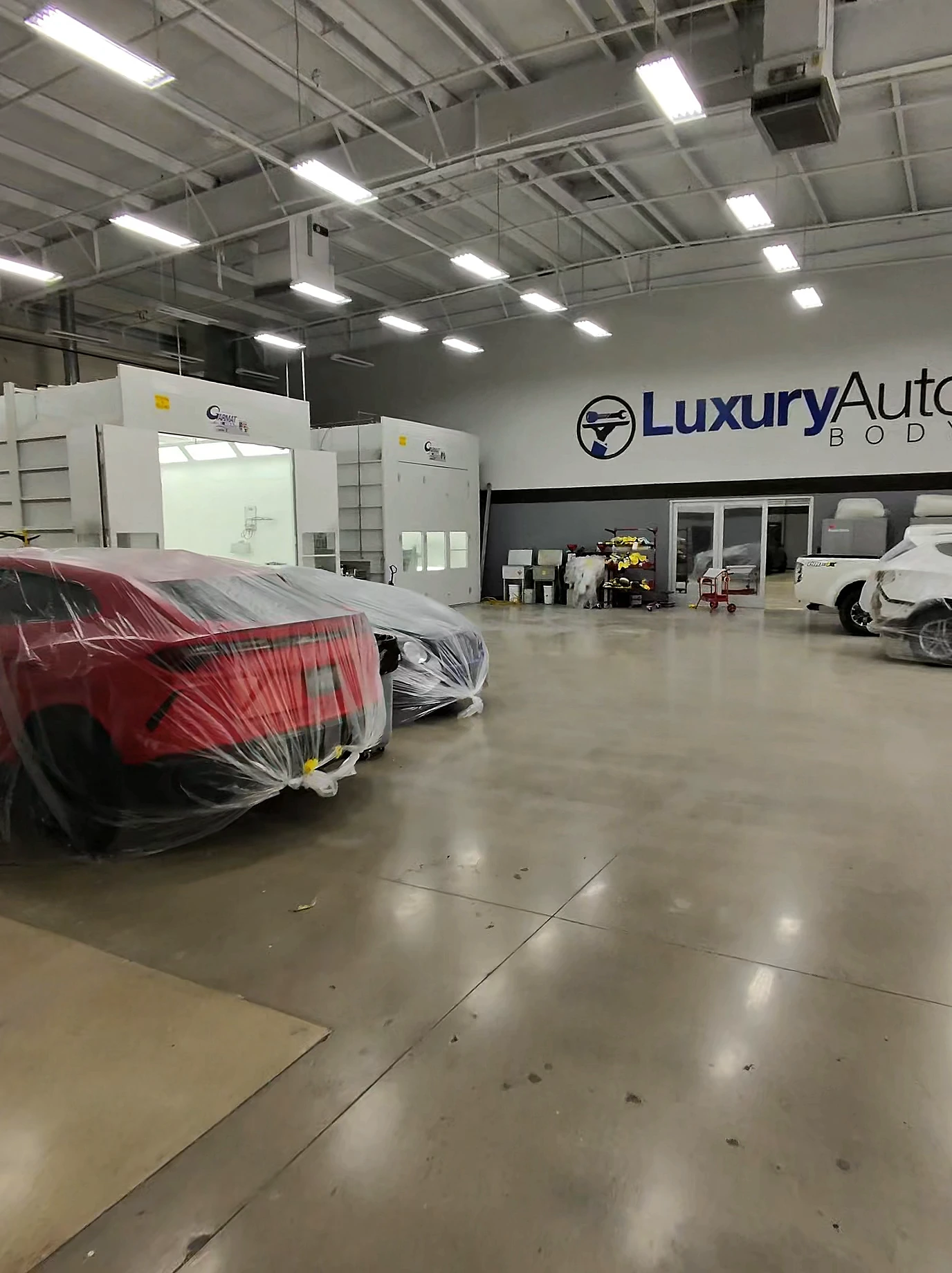 Inside a Luxury Auto Body shop — paint booths beneath the brand sign